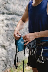 Man adjusting climbing gear with harness outdoors on a sunny day.